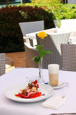 Una mesa de comedor con un plato de comida, un vaso de bebida y un jarrón con una sola flor.