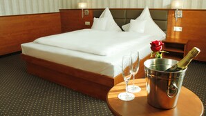 A hotel room with a large bed, two bedside lamps, a small table with a champagne bottle and two glasses, and a vase with a red rose. - Business Hotel Vega (Wroclaw)