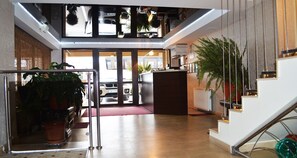 A modern hotel lobby with a reception desk, a staircase, and a view of the street through glass doors. - Hotel Premier (Sibiu)