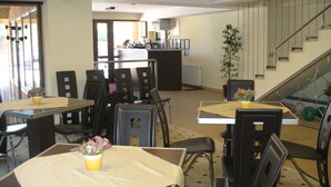 Un área de comedor con mesas y sillas, una escalera y una recepción al fondo.