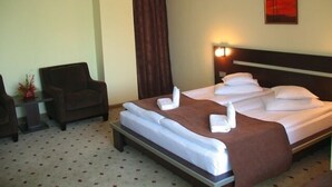 Una habitación de hotel con una cama bien hecha, una silla y una mesita con un florero.