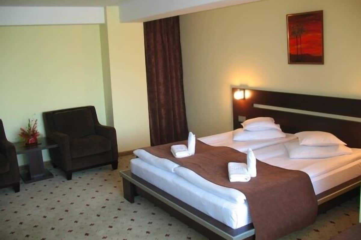 A hotel room with a neatly made bed, a chair, and a small table with a vase.