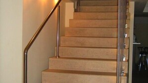 Una escalera con peldaños alfombrados en tonos beige y una barandilla de metal, que conduce a una zona de descanso con un mueble de color oscuro.