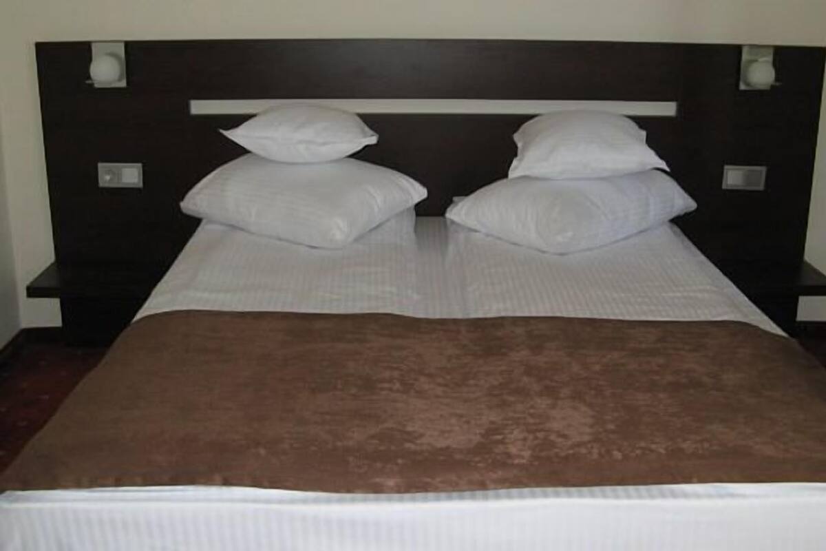 A bed with white linens and a brown blanket, flanked by two bedside tables with lamps.