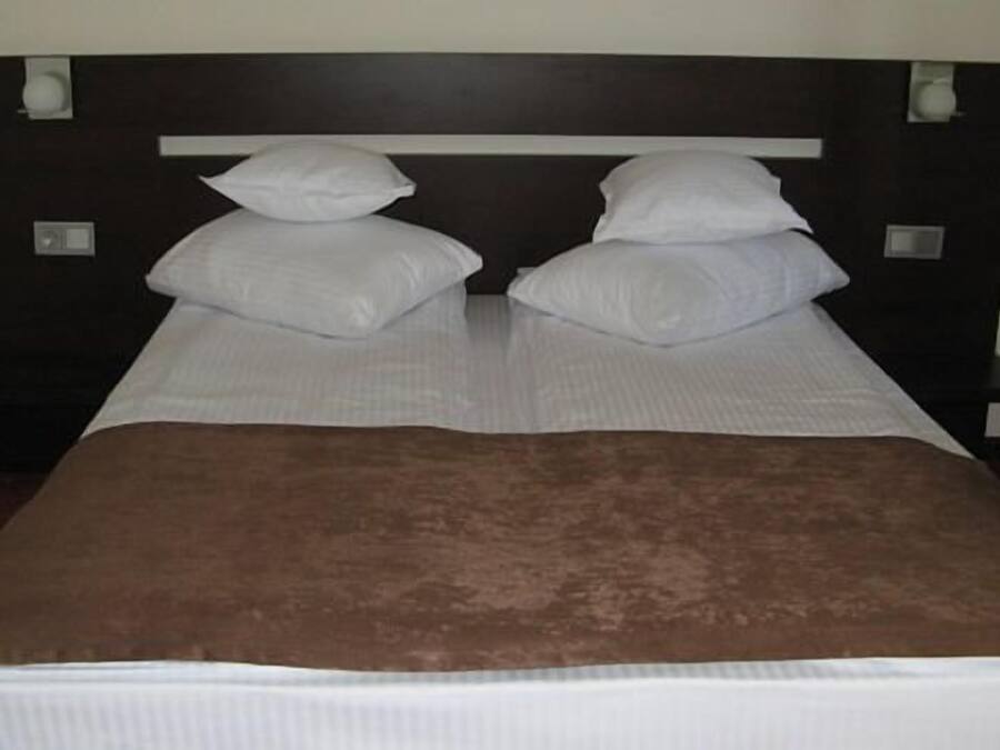 A bed with white linens and a brown blanket, flanked by two bedside tables with lamps.