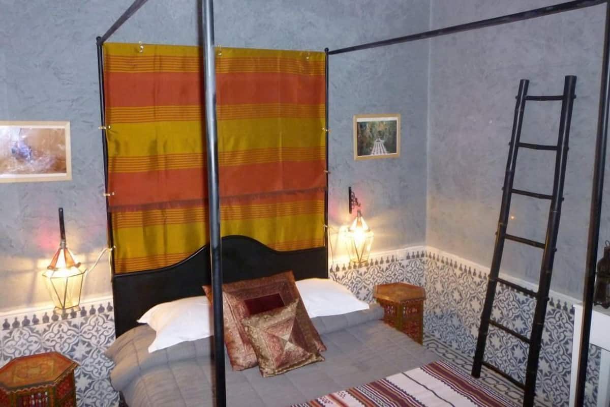 A room with a four-poster bed, a ladder, and patterned walls.