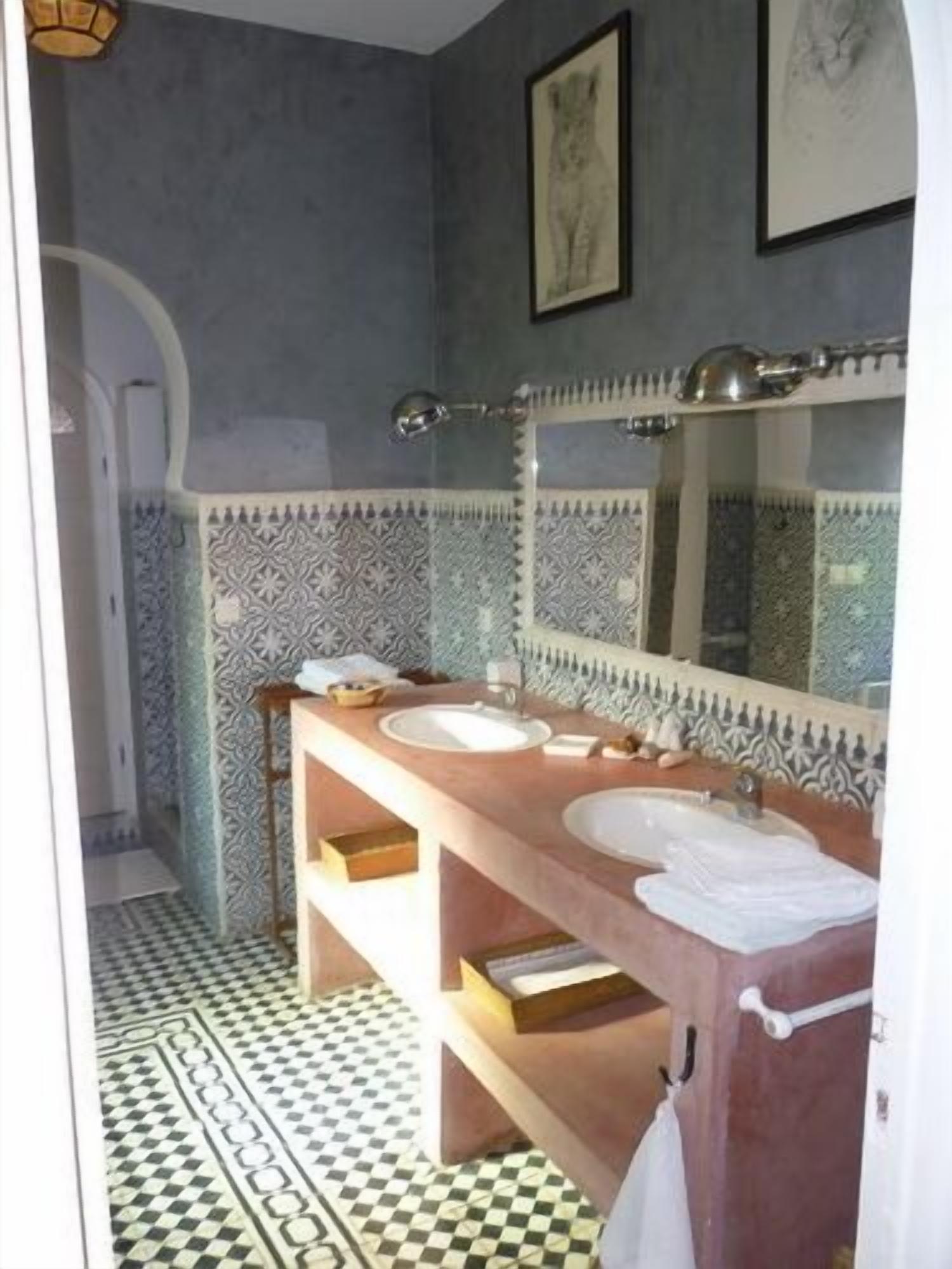 A bathroom with two sinks, a large mirror, patterned tiles, and a checkered floor.