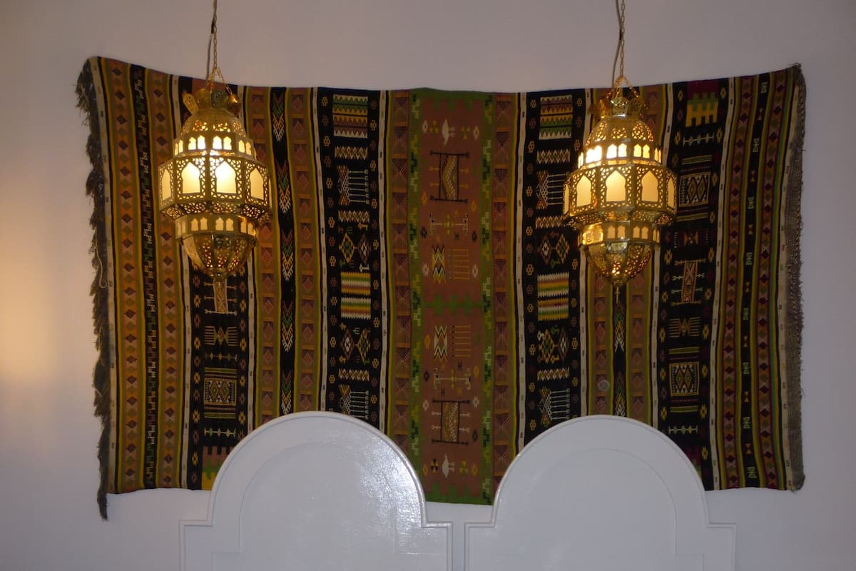 A bed with a patterned bedspread, a white headboard, and two hanging lanterns.