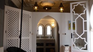 Un pasillo con una puerta blanca, una silla negra, suelo de baldosas y un techo decorativo.