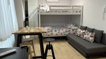 Un espacio habitable compacto con literas, un sofá, una mesita y un taburete.