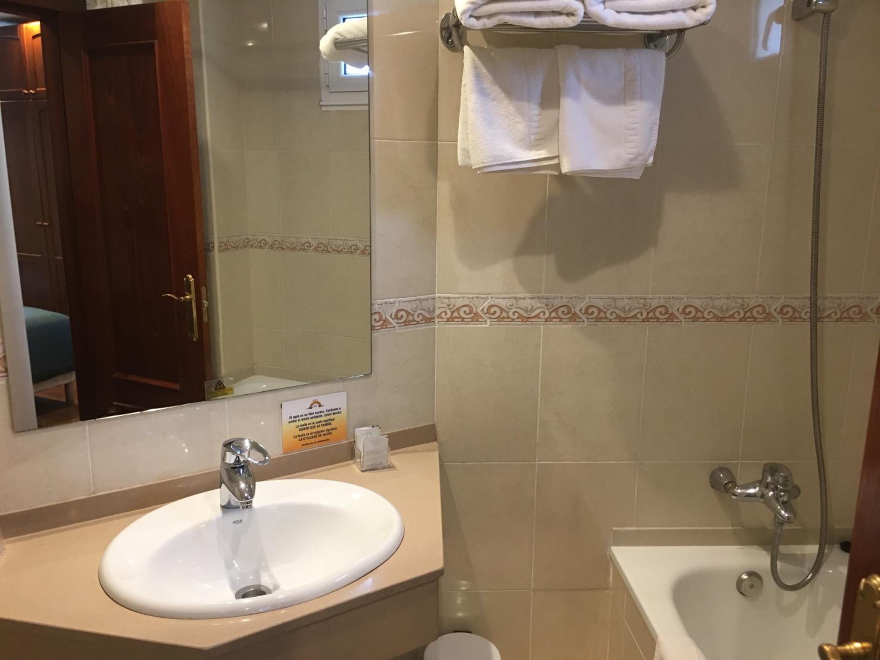 A bathroom with a sink, mirror, towel rack, shower, and toilet.