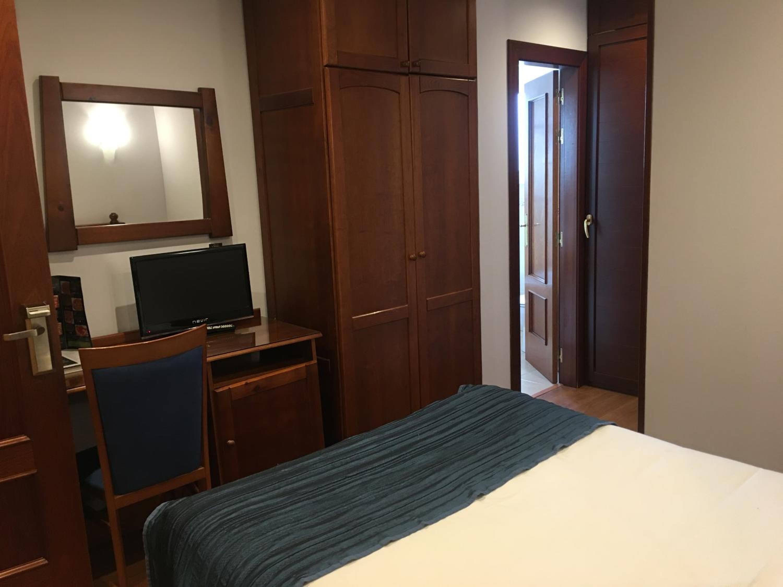 Una habitación de hotel con una cama, un escritorio con ordenador, un espejo y armarios de madera.