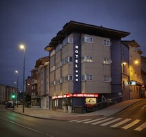Um hotel de vários andares com uma placa grande chamativa com a palavra 'HOTEL' na fachada, uma entrada visível e vista da rua com faixas de pedestres e semáforos.