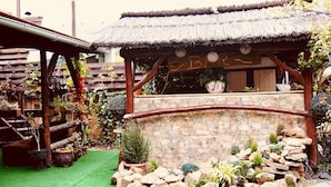 Un espace extérieur rustique doté d’une structure au toit de chaume, de murs en pierre et de diverses plantes en pot.