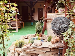 Un jardín rústico con muro de piedra, plantas en macetas y un bebedero metálico para pájaros.