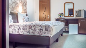 Une chambre à coucher avec un lit, un bureau avec une télévision, une chaise, une armoire et une porte.