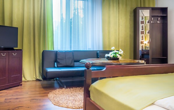Habitación de hotel con cama, sofá, televisión, armario y ventana con cortinas.