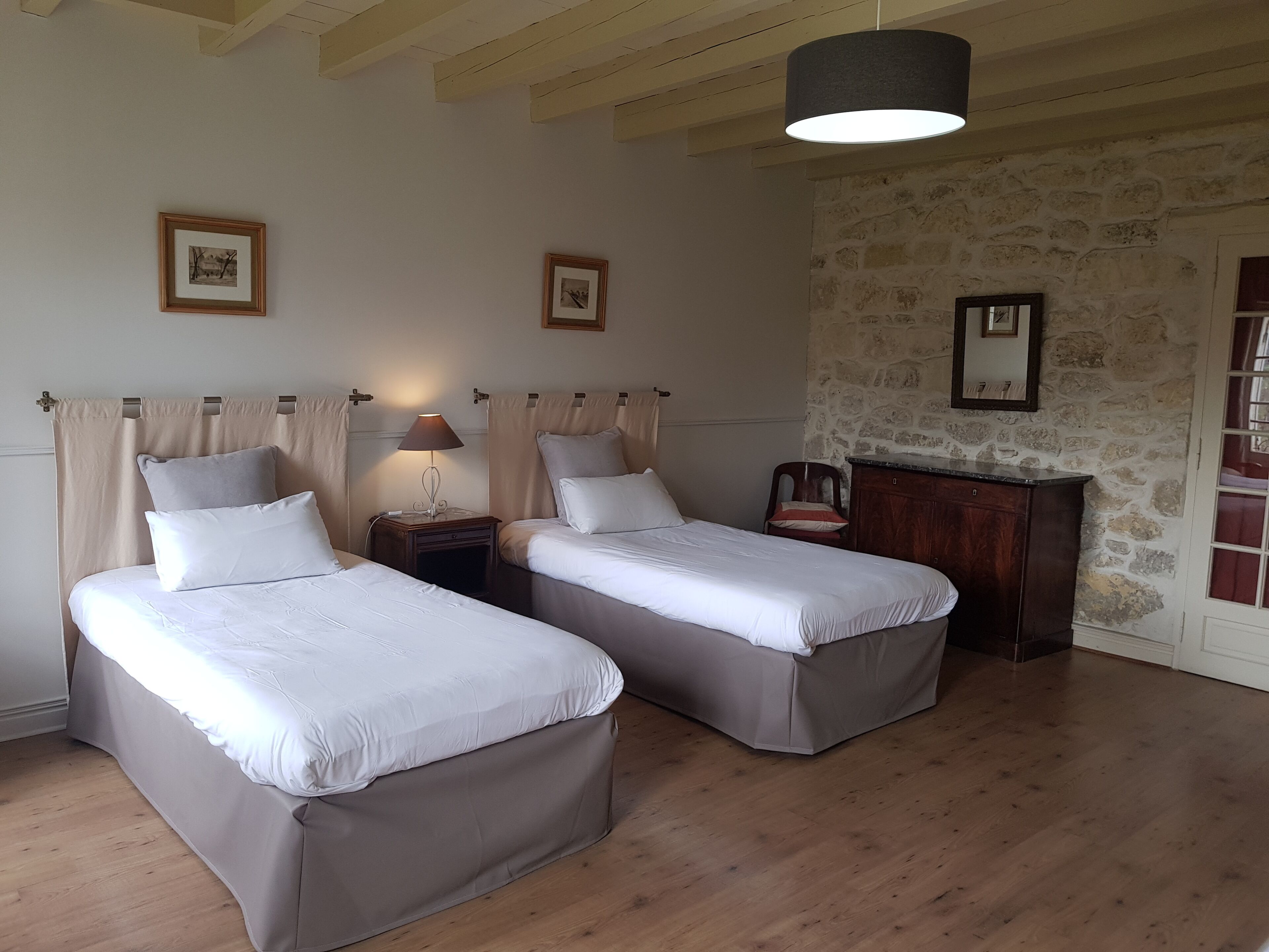 Une chambre avec deux lits, un plancher en bois, un mur en pierre et un luminaire suspendu.