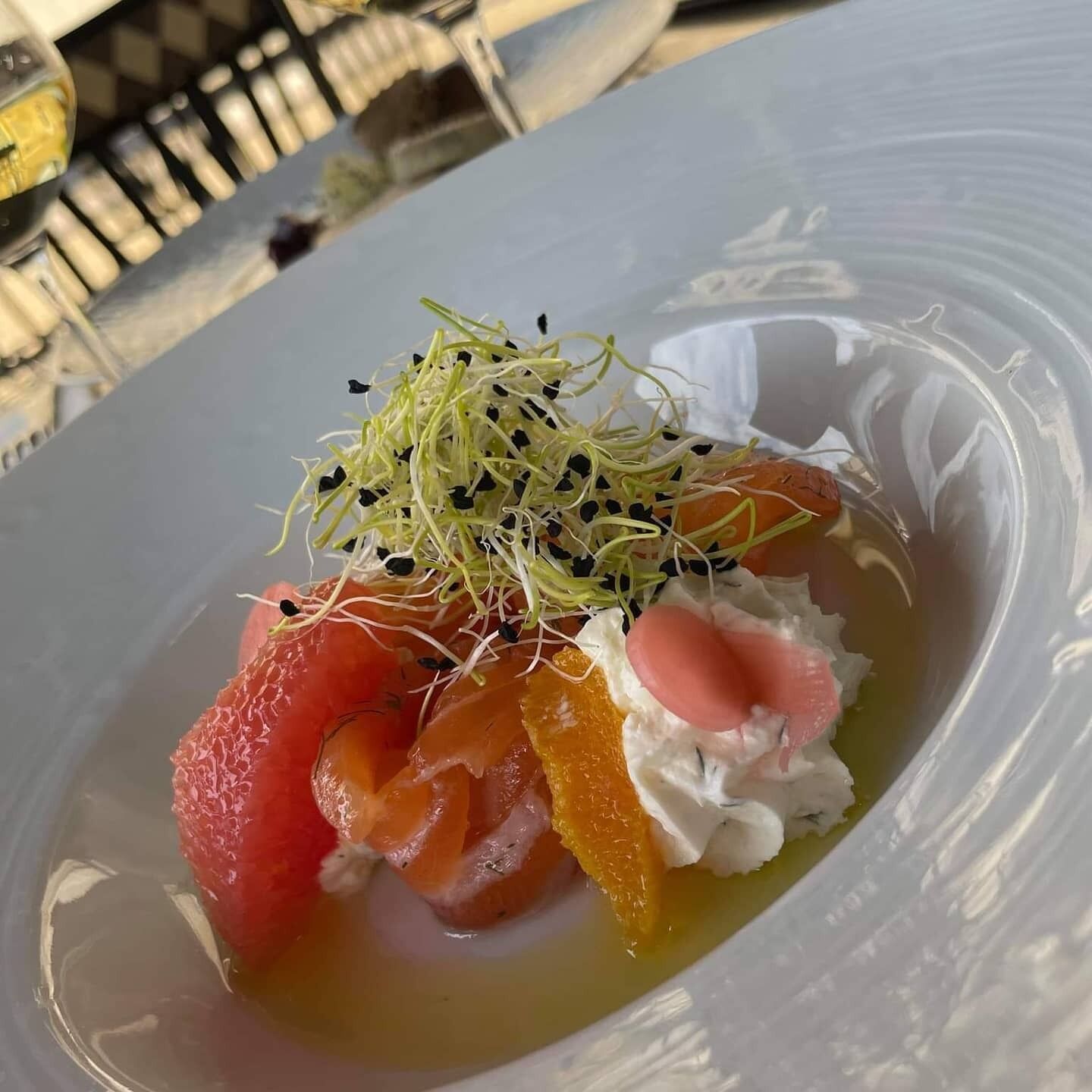 A plate with a dish consisting of salmon, orange slices, and a creamy topping, garnished with sprouts and seeds.