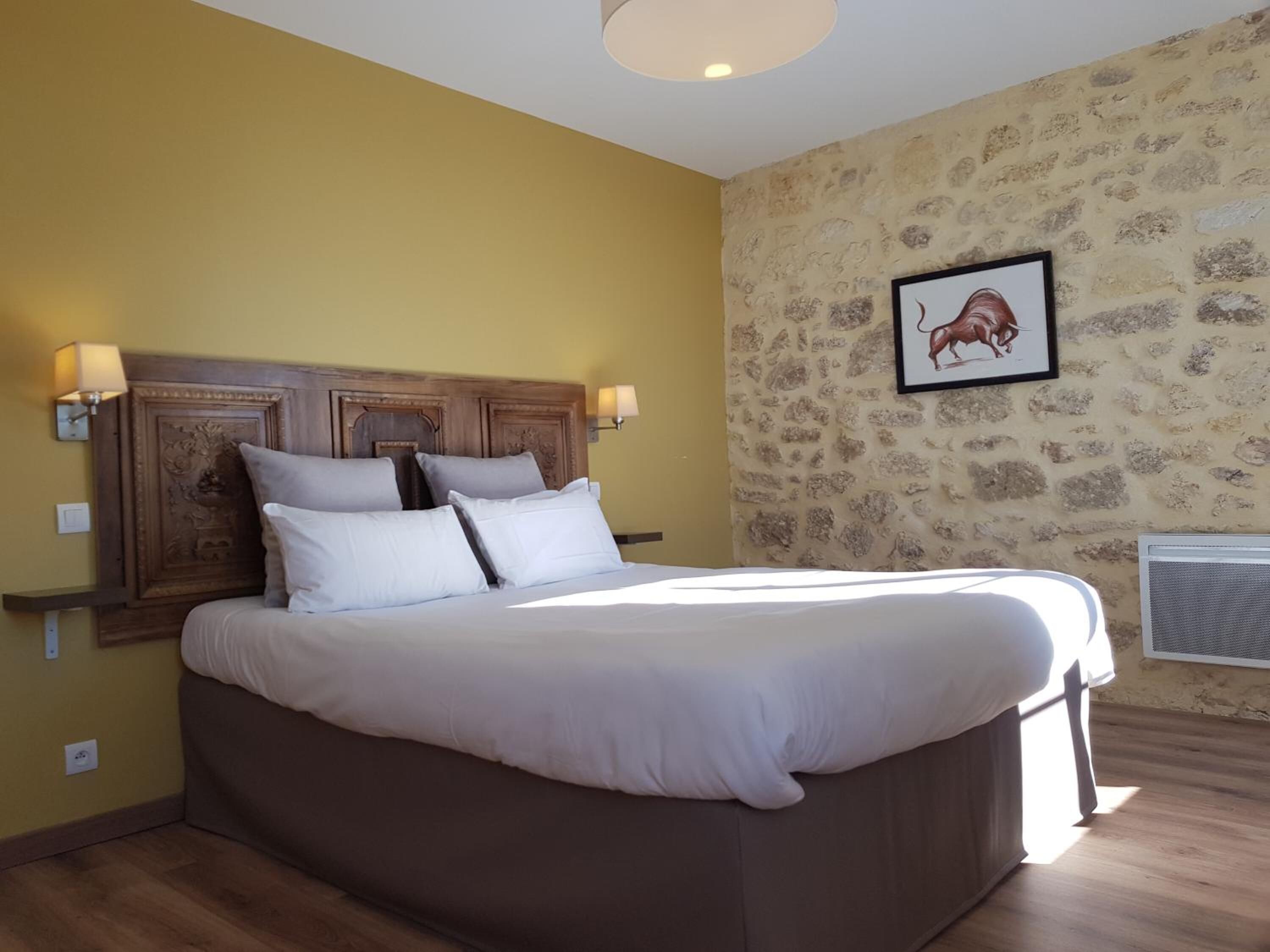 A bedroom with a large bed, wooden headboard, two bedside lamps, and a stone-patterned wall.