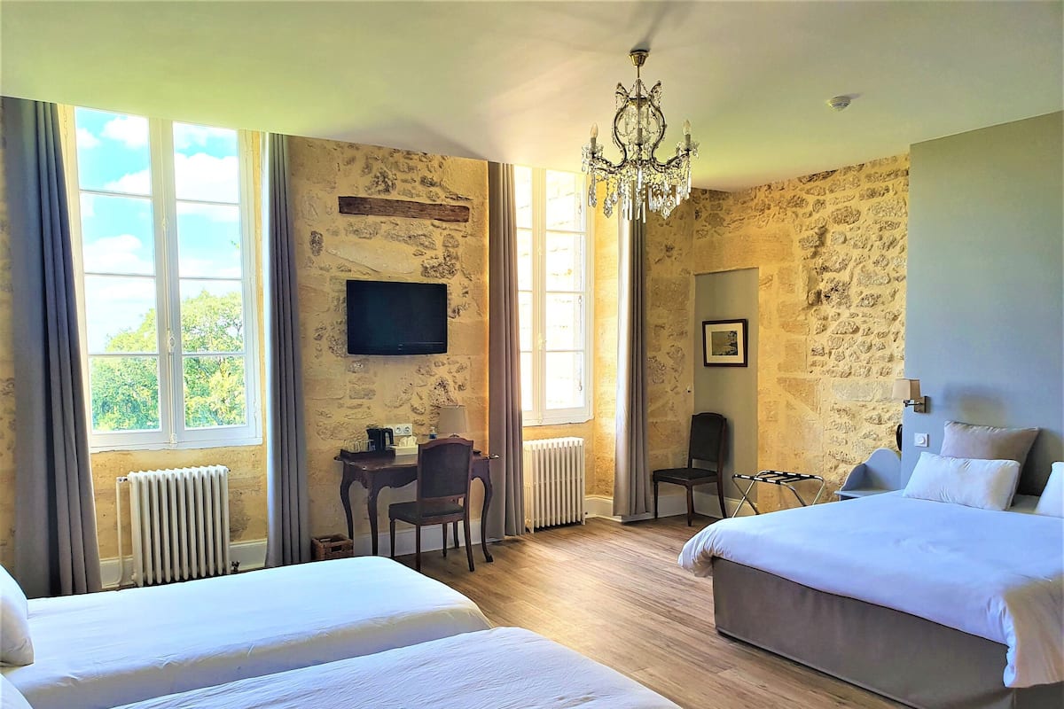 A hotel room with two beds, a desk with a chair, a television, and a chandelier.