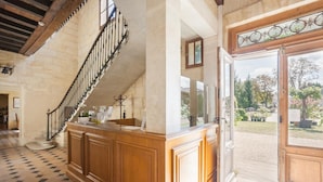 Un magnifique escalier en bois, doté de balustrades noires, mène à une pièce spacieuse où l’on trouve un grand comptoir en bois et, par une porte ouverte, une vue sur un jardin.