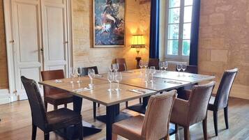 A dining room with a large rectangular table set for six, surrounded by wicker chairs. There is a chandelier above the table and a painting on the wall.