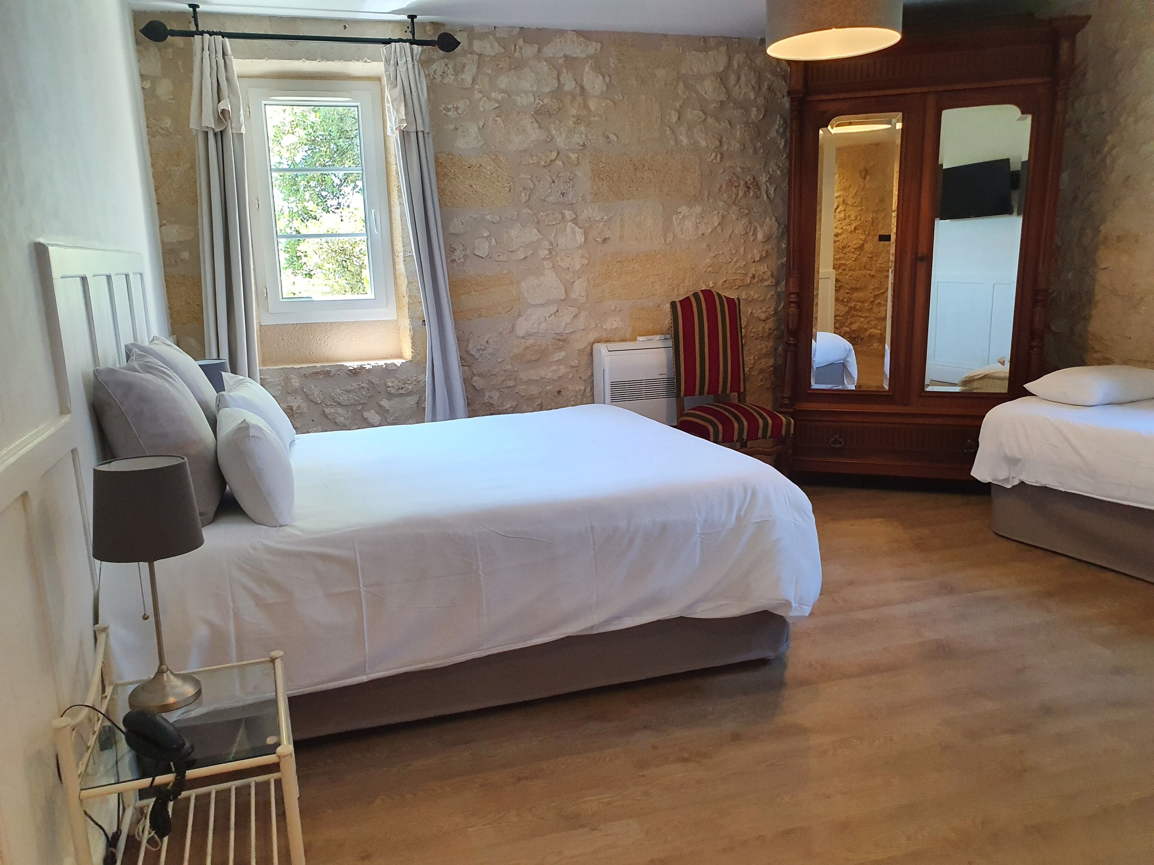 A bedroom with a large bed, a chair, a mirror, and a wardrobe.