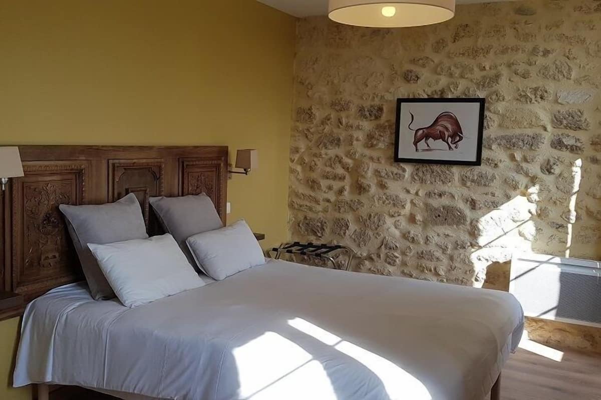 A bedroom with a stone wall, a bed with a wooden headboard, and a framed picture of a pig.