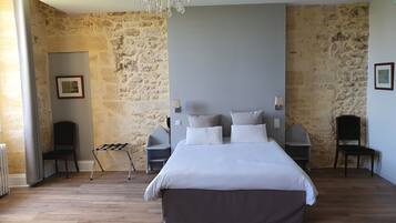 A bedroom with a large bed, a chandelier, stone walls, and a framed picture on the wall.
