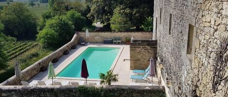 A pool area with stone walls, lounge chairs, and umbrellas.