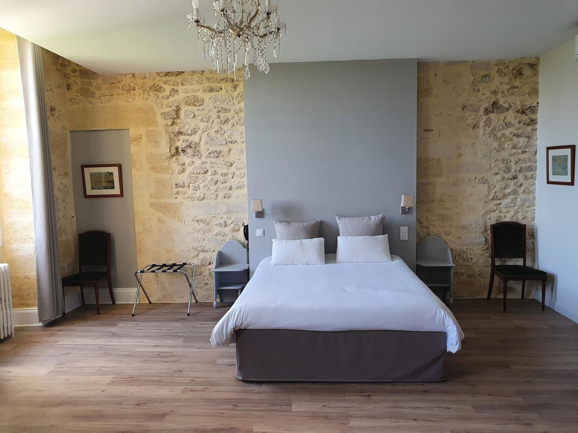 A bedroom with a large bed, two bedside tables, a chandelier, stone walls, and a radiator.