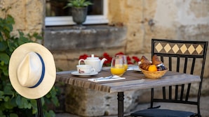 Une table avec une théière, des tasses, un verre de jus d’orange et un panier de pain et de fruits.