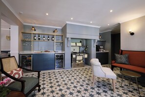 A modern kitchen with a bar area, a seating area with a sofa and chairs, and a patterned floor.