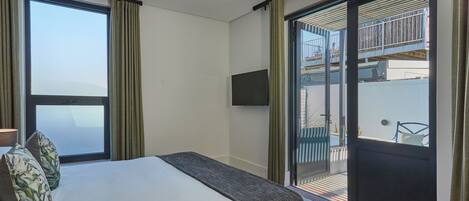Habitación de hotel con cama, televisor montado en la pared y puerta corredera de vidrio que da a un espacio exterior.