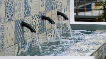 Ein Wasserspiel mit drei gebogenen Ausläufen vor einer mit aufwendigen Mustern versehenen Wand.