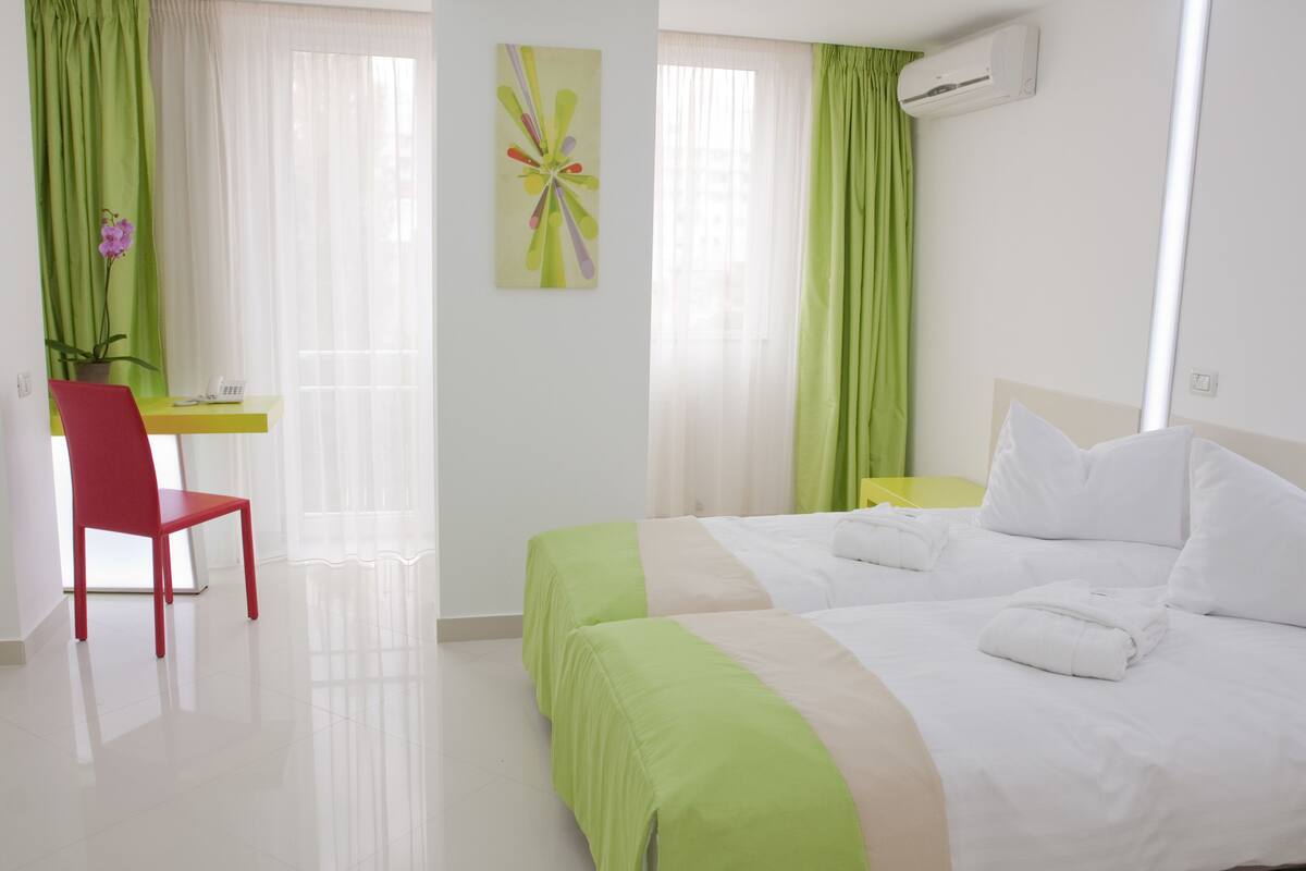 A hotel room with a bed, a desk, a chair, and a potted plant.