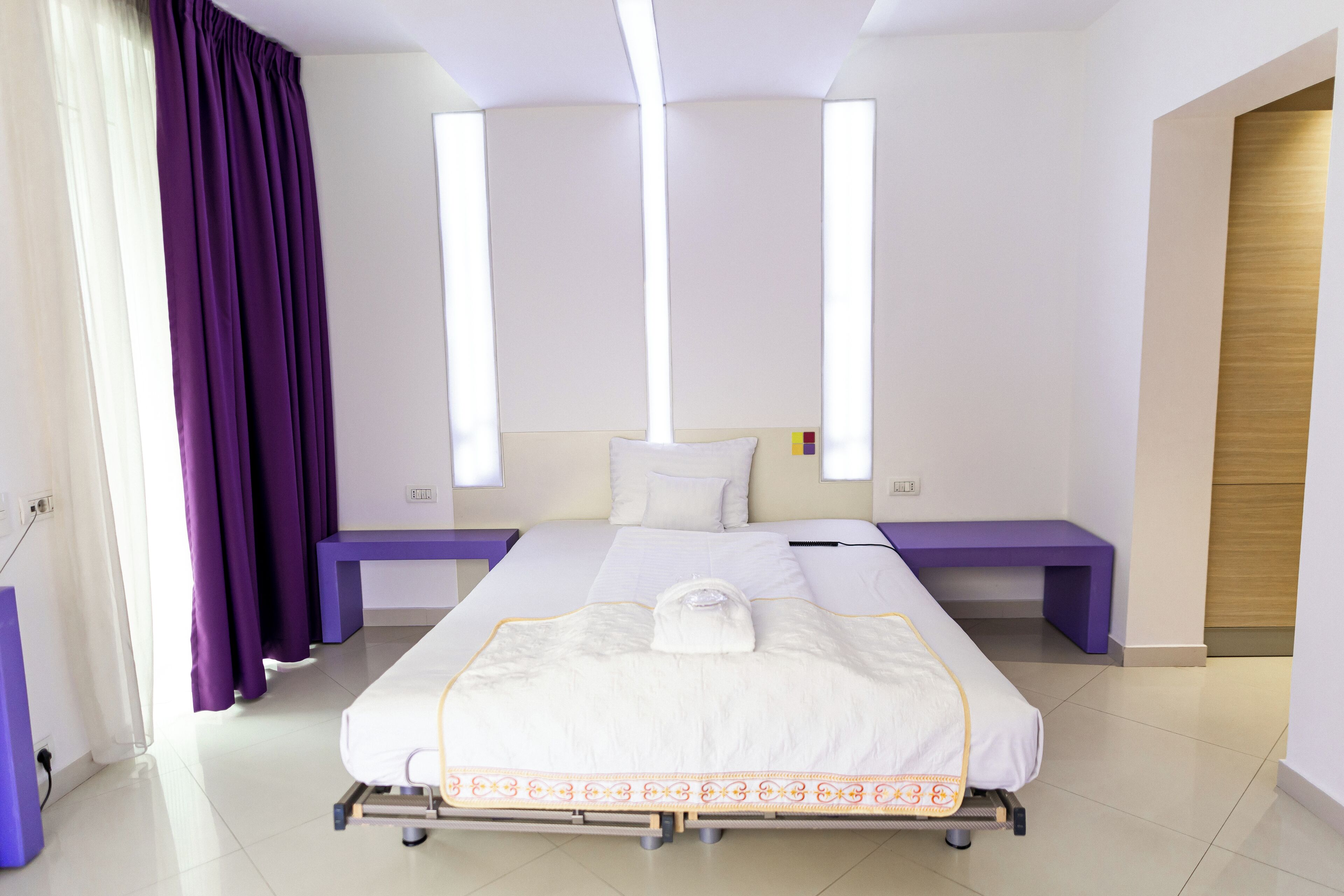 Et hotelværelse med seng, sengeborde, bænk og dør til badeværelse.