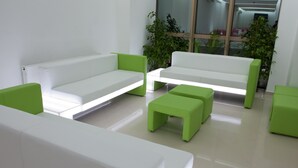 Un espace d’attente moderne avec des canapés blancs et des touches de vert, comprenant une petite table et un pouf.