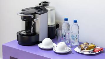 Una mesa morada con una cafetera, dos botellas de agua, un plato con comida y dos tazas blancas.