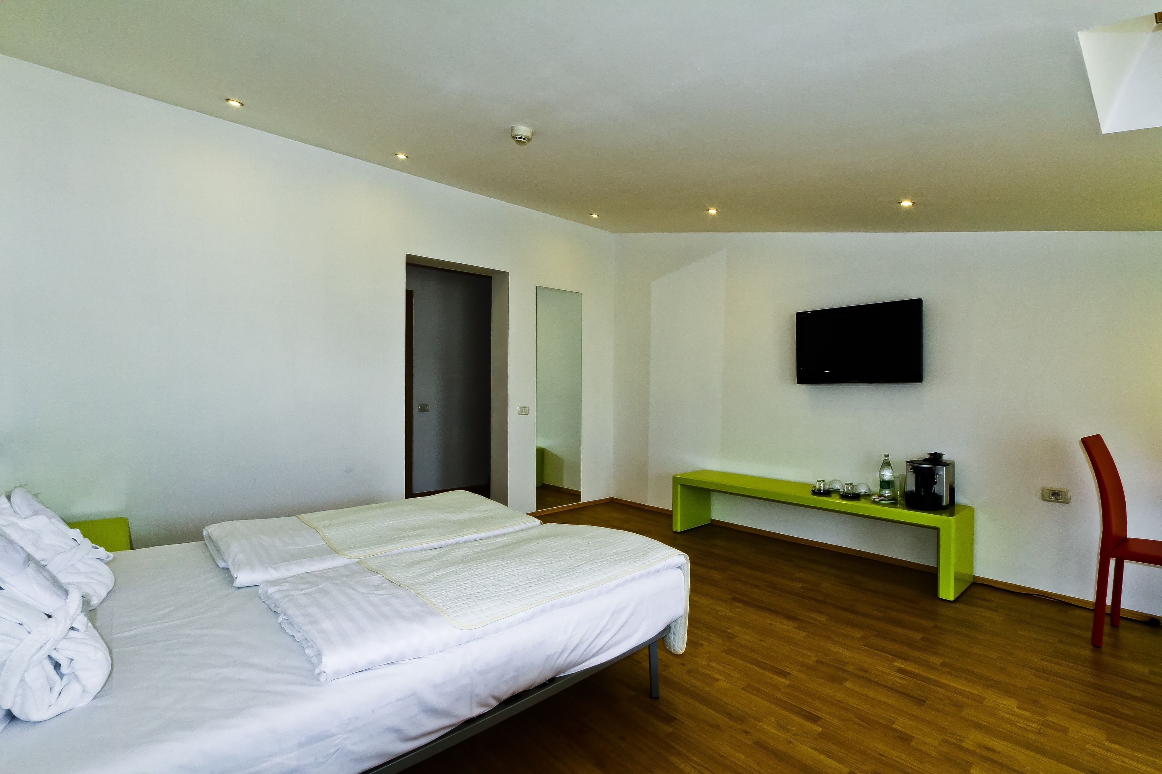 A hotel room with a bed, a bench, a TV, and a chair.