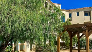 A courtyard with a pergola, a large tree, and a building with a tiled roof. - Les Pavillons du Golfe (Conca)