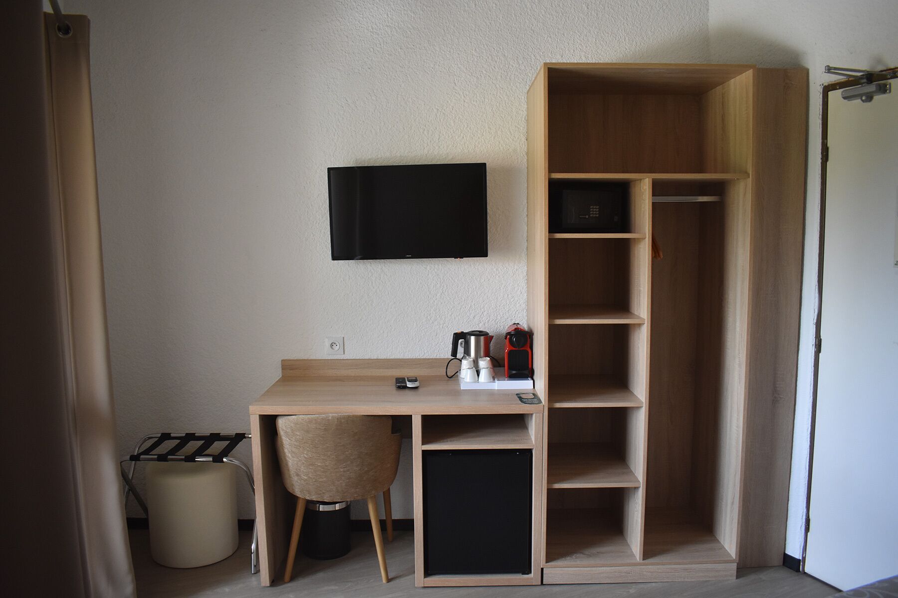 A compact room with a desk, chair, and a TV mounted on the wall.