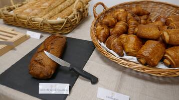 A display of baked goods including bread, croissants, and a loaf of cake with a knife on a black cutting board.