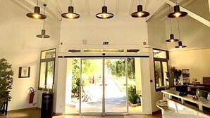 A spacious lobby with a high ceiling, multiple pendant lights, a reception desk, and a glass door leading outside. - Les Pavillons du Golfe (Conca)
