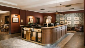 A reception area with a wooden reception desk, framed pictures on the wall, and a patterned rug. - Andrássy Kúria & Spa (Tarcal)