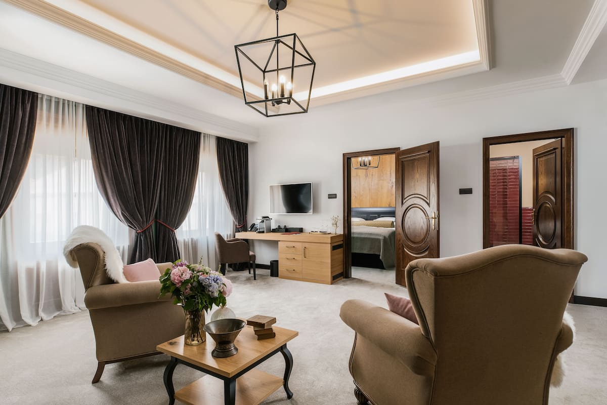 A modern hotel room with a sofa, armchair, desk, and a television.