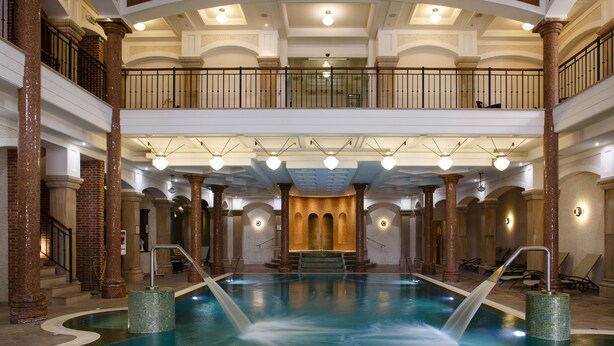 A large indoor swimming pool with a central waterfall feature, multiple levels with balconies, and classic architectural elements like columns and arches. - Andrássy Kúria & Spa (Tarcal)