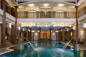 A large indoor swimming pool with a central waterfall feature, multiple levels with balconies, and classic architectural elements like columns and arches. - Andrássy Kúria & Spa (Tarcal)