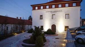 A white building with "ANDRÅSSY REZIDENCIA" on the facade, featuring a central entrance, a brick roof, and a paved courtyard with a circular garden. - Andrássy Kúria & Spa (Tarcal)